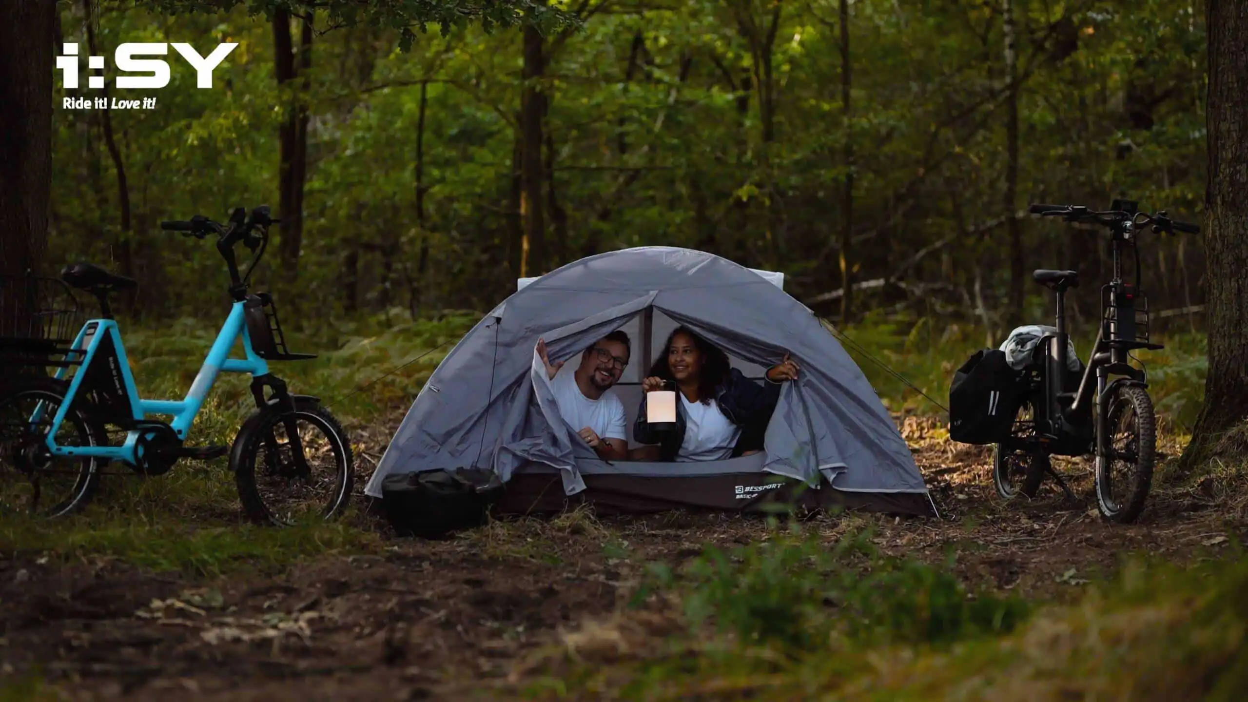 Paar zeltet und schaut aus Zelt heraus, i:SY Räder stehen daneben – Szene aus einem Werbefilm für die Firma i:SY GmbH & Co. KG, produziert von Charlie Grashoff - The C/A Studio, Videoproduktion in Leipzig. Projekte deutschlandweit. Imagefilme, Corporate Videos, Brandfilme, Eventfilme, Industriefilme & mehr. Location Scouting. Drehorte. Shooting Locations. Orte für Dreharbeiten.