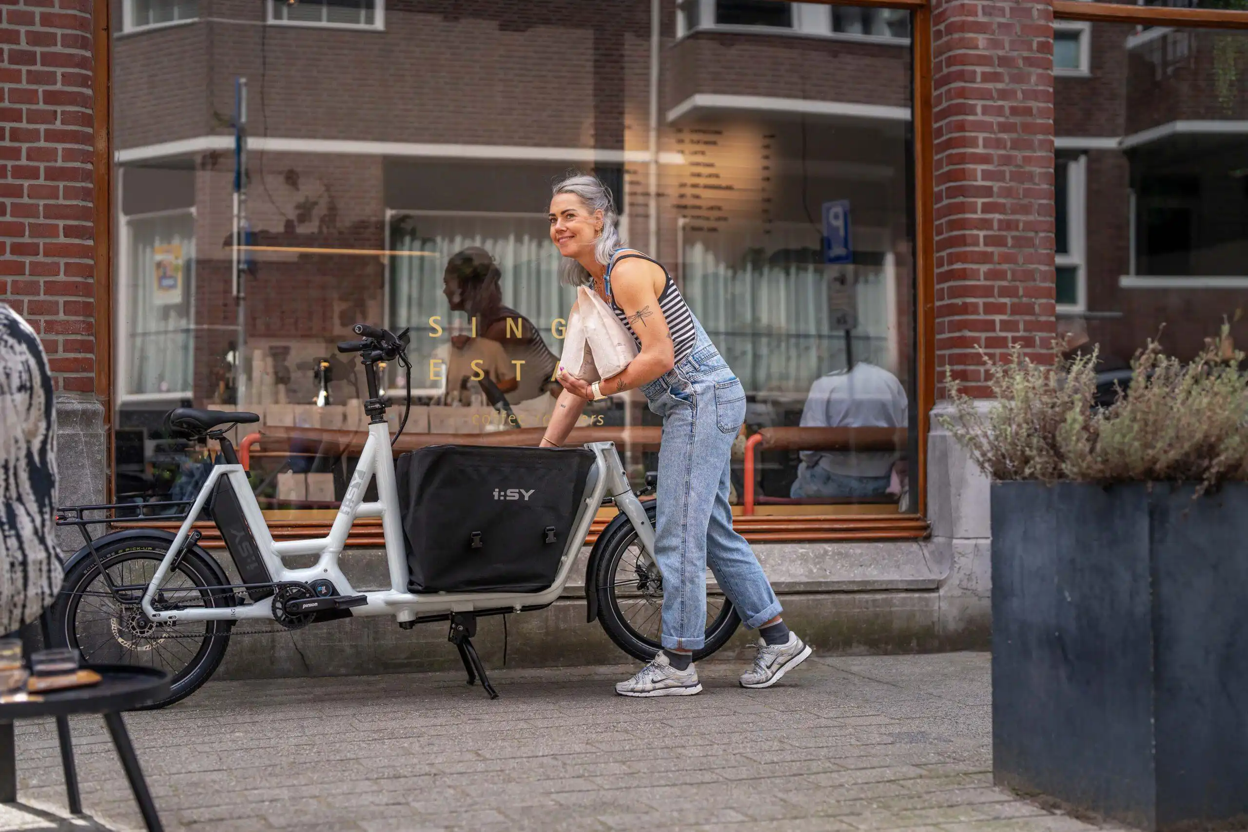 Person mit i:SY E-Bike vorm Single Estate Coffee in Den Haag – Szene aus einem Werbefilm für die Firma i:SY GmbH & Co. KG, produziert von Charlie Grashoff - The C/A Studio, Videoproduktion in Leipzig. Projekte deutschlandweit. Imagefilme, Corporate Videos, Brandfilme, Eventfilme, Industriefilme & mehr. Fotografie Leipzig. Werbefilm Produktion.